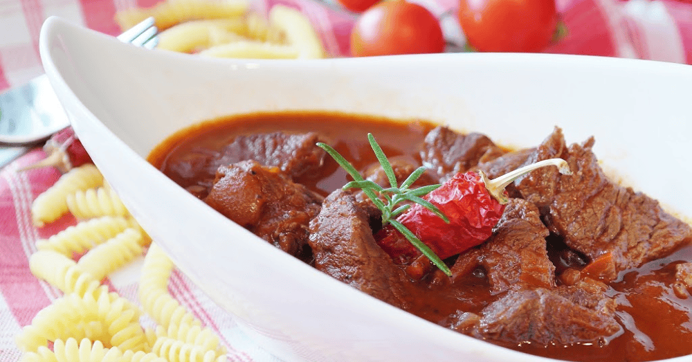 Hearty beef chili served with pasta and fresh herbs on a cozy table setting.