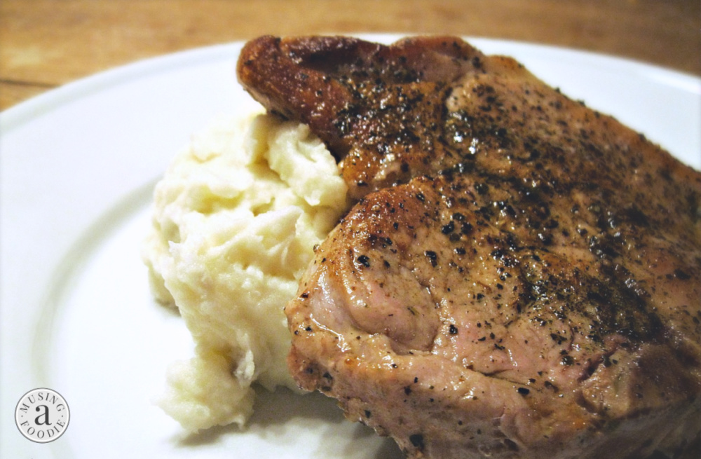 Seared juicy pork chops served with mashed potatoes on a plate.