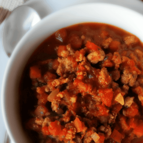 Hearty no-bean pork chili served in a rustic white bowl, perfect for comfort food lovers.