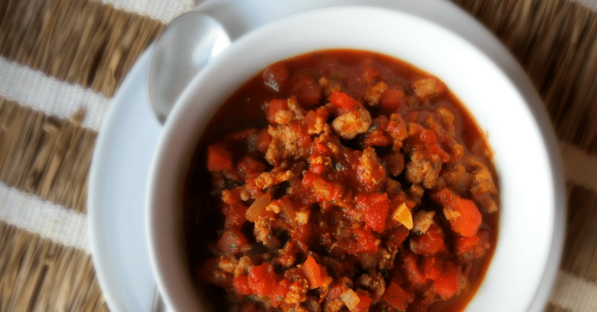 Hearty no-bean pork chili served in a rustic white bowl, perfect for comfort food lovers.