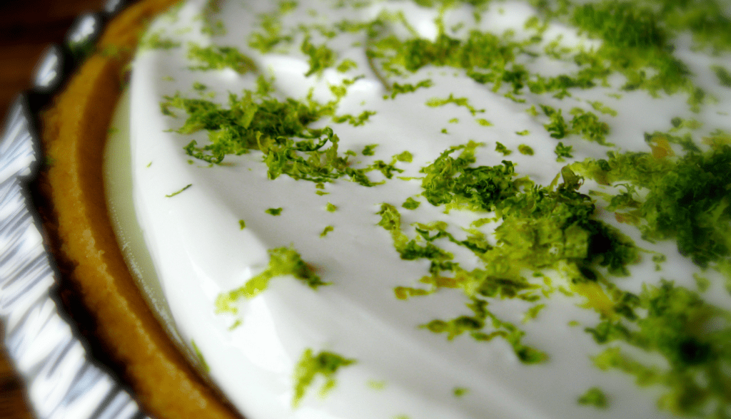 Close up shot of homemade key lime pie with a sour cream topping and fresh lime zest.
