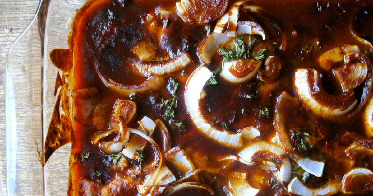 Delicious BBQ pork chops topped with caramelized onions and fresh herbs in a glass baking dish.