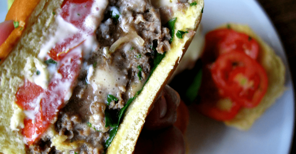 Close up shot of a sliced cheese stuffed slider topped with mayonnaise, tomato, and fresh spinach.