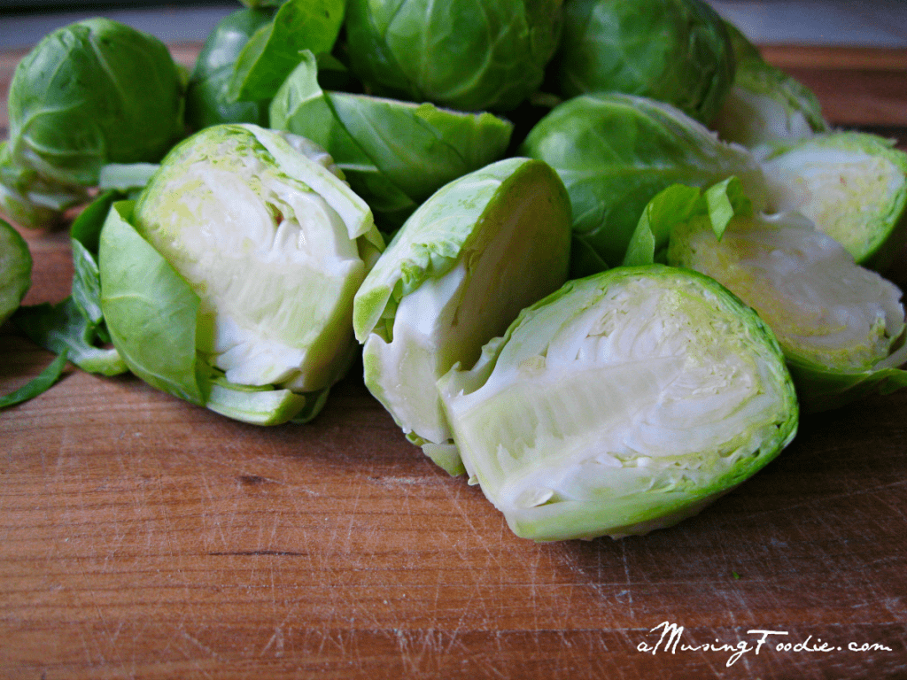 Raw brussels sprouts cut in half on a wooding cutting board.
