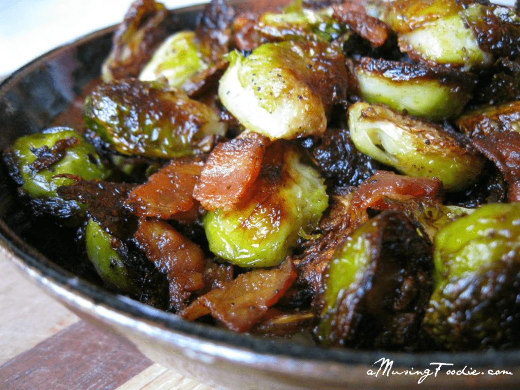 Roasted brussels sprouts with bacon in a brown ceramic bowl on a wooden cutting board.