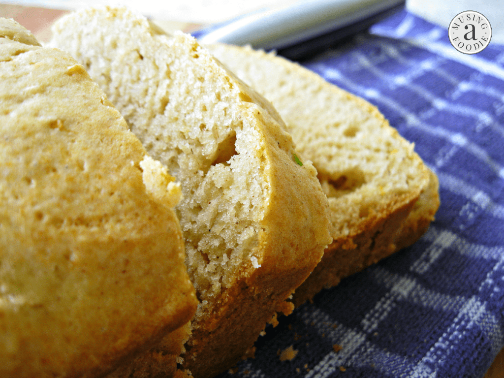 Honey lemon zucchini bread loaf on a blue and white towel, with two slices cut.