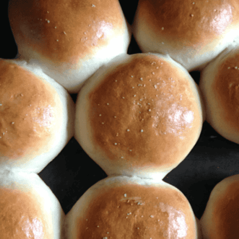 Freshly baked golden bread rolls on a dark tray, invitingly soft and fluffy.