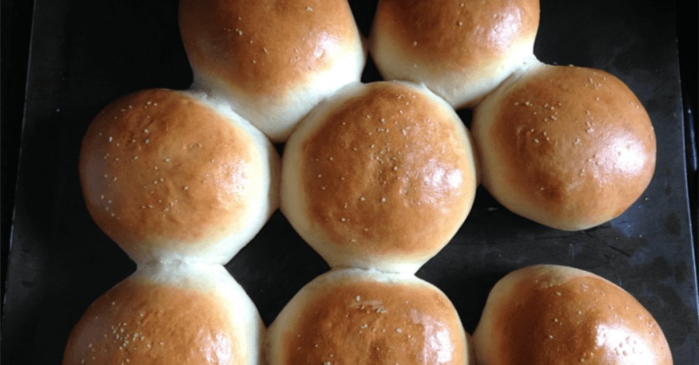 Freshly baked golden bread rolls on a dark tray, invitingly soft and fluffy.