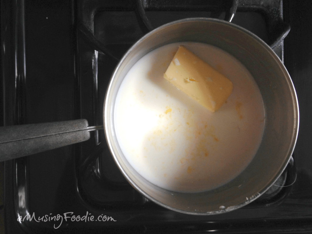Overhead view of butter melting in milk in a pot on a gas range.