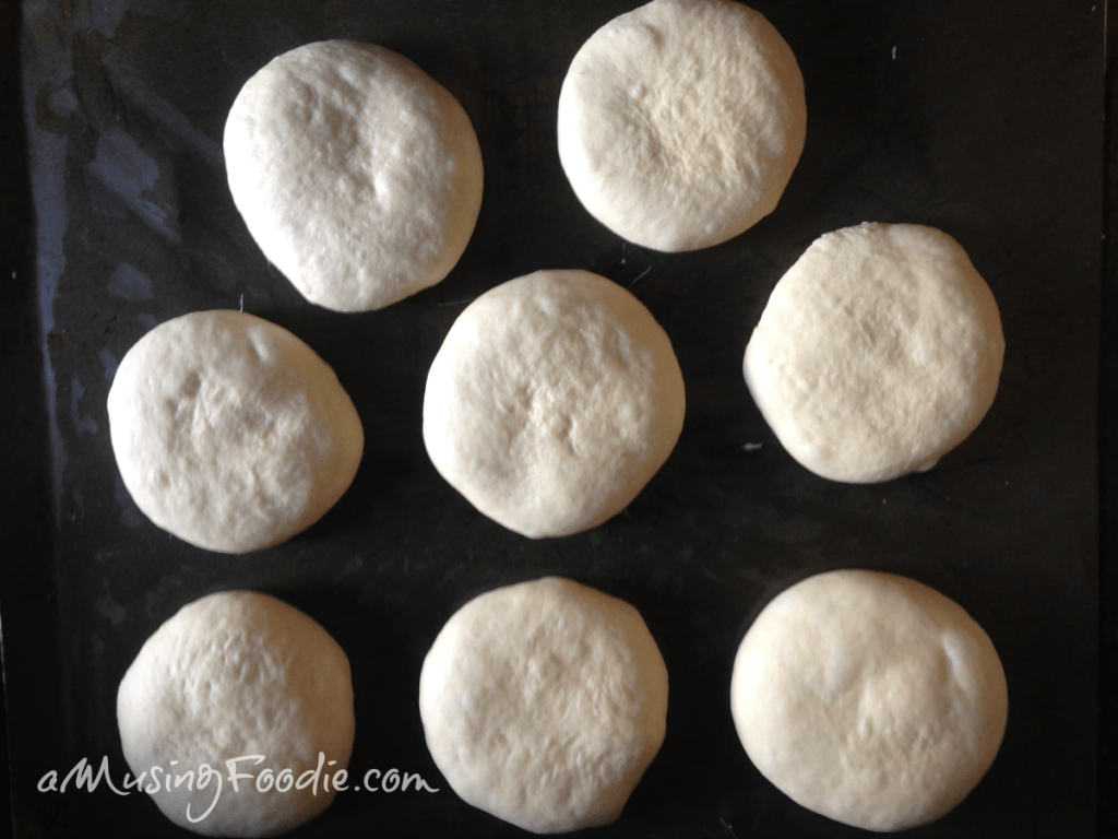 Eight rounds of dough sitting on top of a dark counter.