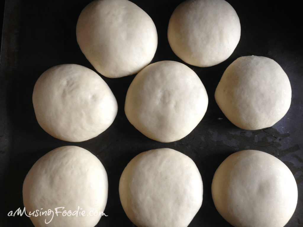Eight rounds of dough sitting on a dark table.