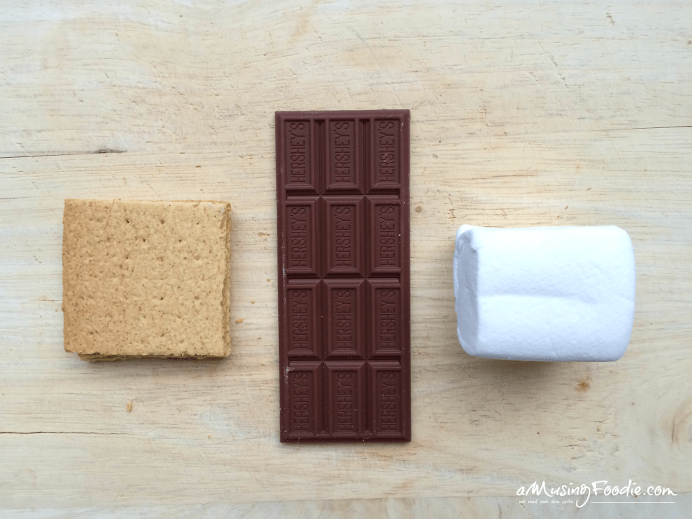 Graham cracker, chocolate bar and large marshmallow on a wooden cutting board.