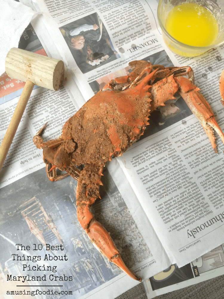 Steamed blue crab with Old Bay on a newspaper. A crab mallet is to the left and a glass cup of melted butter is on the right.
