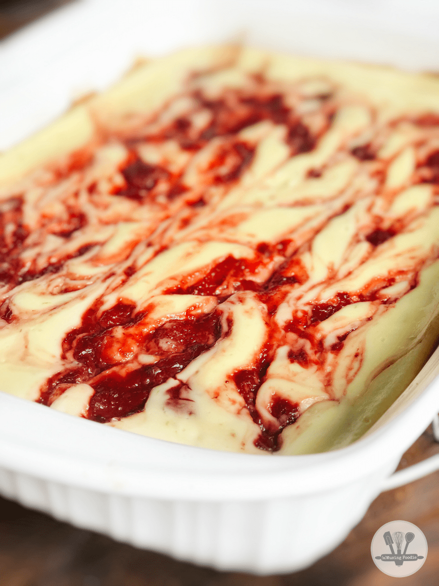 Cheesecake with strawberry swirls in a white baking dish.