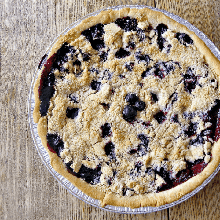 Freshly baked blueberry peach pie with golden streusel topping in a rustic setting.