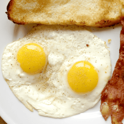 Delicious breakfast with sunny-side-up eggs, crispy bacon, and golden-brown toast on a plate.