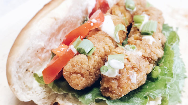 Close up of crispy chicken strips layered on a sub roll with a lemon mayo sauce, lettuce, tomato and green onion.