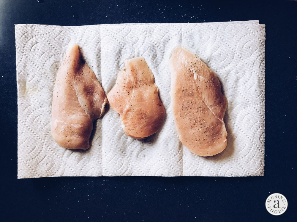 Three raw chicken breasts seasoned with salt and pepper.