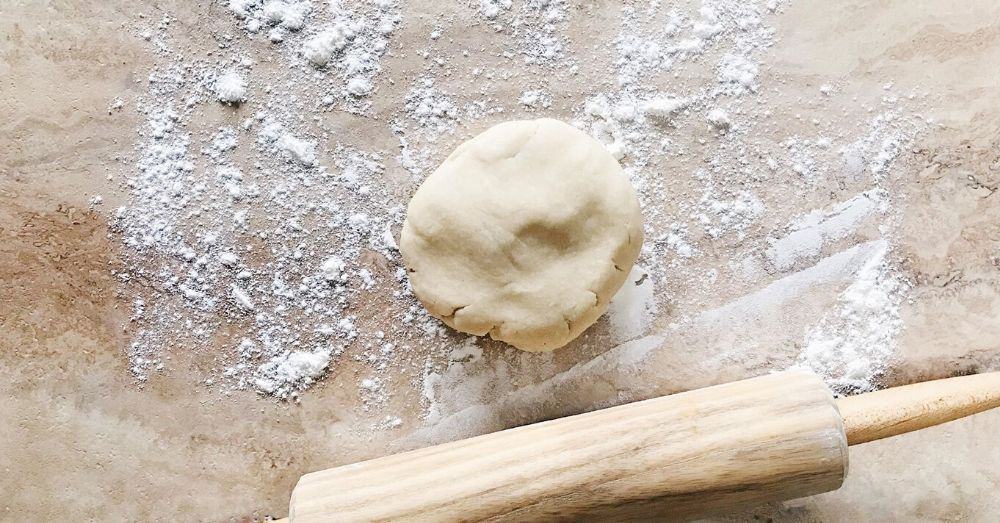 Buttery pie dough ball on a floured surface with a wooden rolling pin.