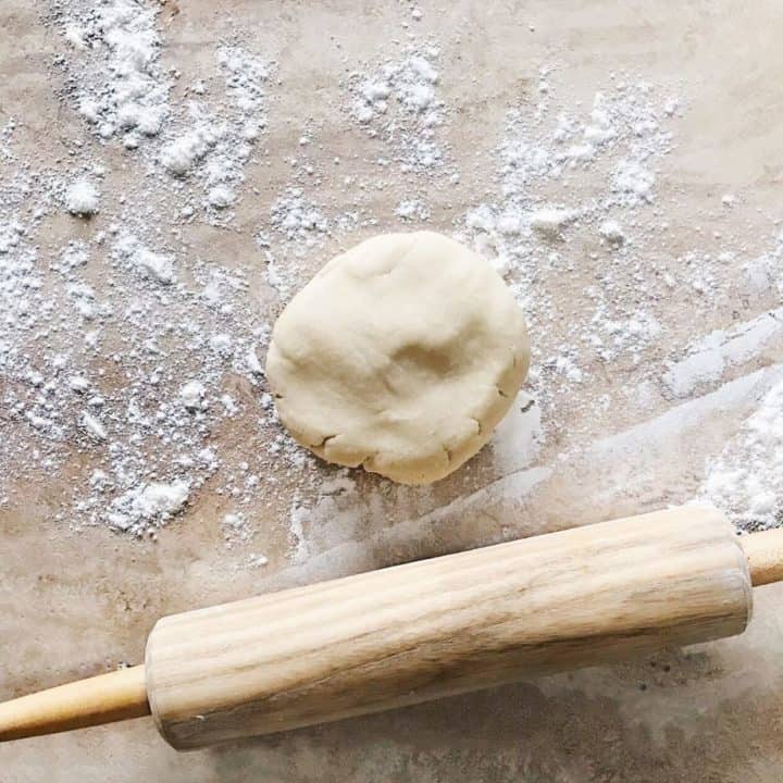 Handcrafted pie dough on a floured wooden counter with a classic rolling pin.
