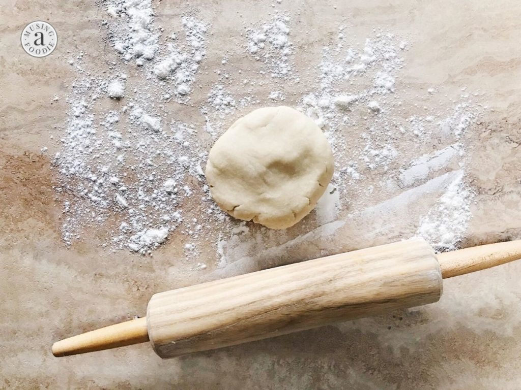 Disk of pie dough on a floured counter with a rolling pin.