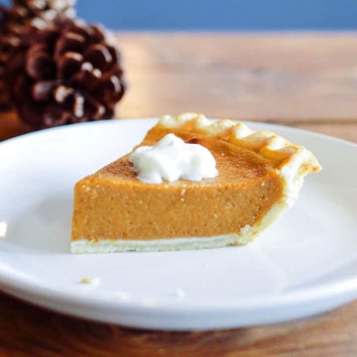 Homemade pumpkin pie slice topped with whipped cream on a rustic wooden table.
